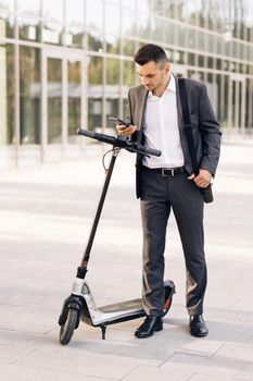 A male businessman approaches an electric scooter and using mobile phone app. Ecological transportation. Man uses an electric scooter as a modern means of transportation in the city.