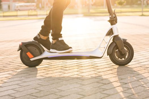 Fast speed driving electric transport. Man hipster riding an electric scooter. Eco-friendly transportation. Shot on legs young hipster man in black sneakers ride on electric mobile scooter at sunrise