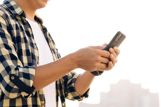 Man stand in the city center street uses phone texting scrolling tapping smile technology communication sunny day success slow motion. He's browsing the web on his device