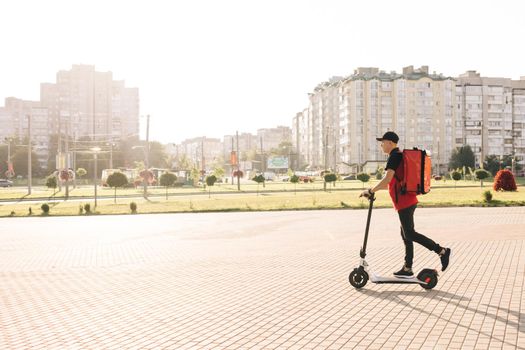 Deliveryman worker employee in red uniform. Asian man courier food delivery with red thermal backpack rides the street on an electric scooter deliver online order client customer. Excellent delivery.