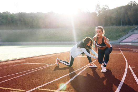 Athlete exercises with personal trainer standing on start on stadium, then rushing forward, getting ready for competition. Female athlete on track. Exercising strength, cardio and power