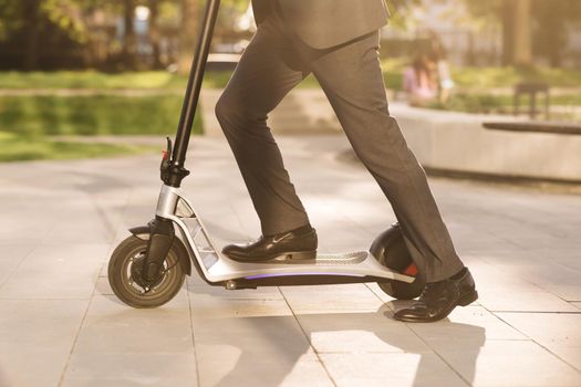 Close up of legs man in suit riding electric scooter in city. Unknown businessman in classic suit ride on electric mobile scooter. Modern eco friendly transport. Fast speed driving electric transport.