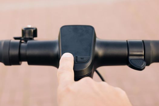 Close up of hipster man turns on the electric scooter. Male is pushing start button of modern gadget and driving along street of city. Hands of a young man close-up. Ecological alternative transport.