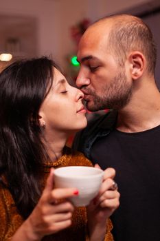 Portrait of happy boyfriend kissing girlfriend on nose celebrating christmas holiday together spending time together in xmas decorated kitchen. Joyful couple enjoying winter season.