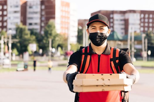 Young male food courier wearing protective mask while walking down city street with insulated red backpack delivering order. Delivery services. Excellent delivery.