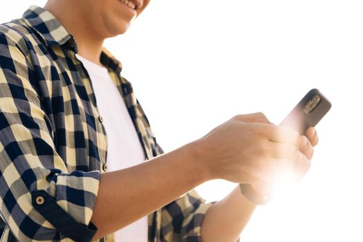 Hipster man in shirt is using a smartphone on a street in downtown. He smiles and looks successful. He's browsing the web on his device.