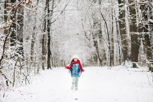 Happy child girl plays with a snow in winter day. Girl enjoys winter, frosty day. Cute little happy girl in winter clothes is having fun running in snowy winter day.