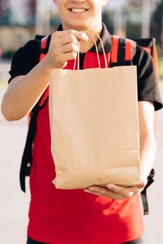 Happy delivery worker holding packet with food looking at the camera and smiling. Close up portrait of positive young man courier person. Delivery service door to door.