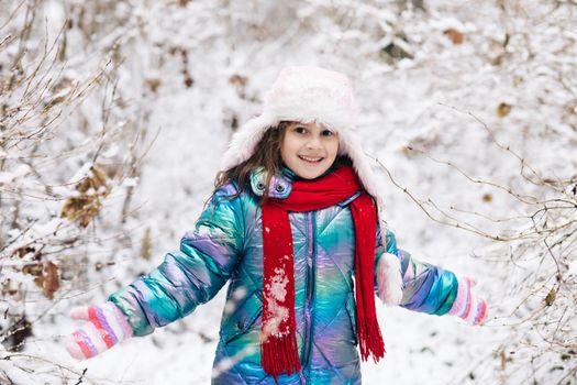 Happy child girl plays with a snow in winter day. Girl enjoys winter, frosty day. Playing with snow on winter holidays. Walk in winter forest.