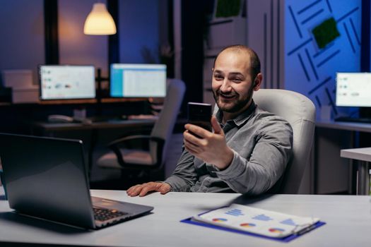 Happy freelancer sitting at desk discussing on online call using smartphone. Businessman in the course of an important video conference while doing overtime at the office.