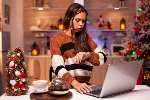 Angry person working on christmas eve night using laptop computer technology at festive home. Young woman on virtual network for business project, upset adult about wasting time