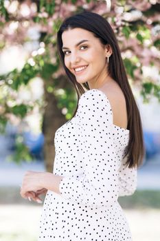 European girl is moving down the park, then she turns the camera. Girl with pink cherry blossom petals in cherry blossom forest.