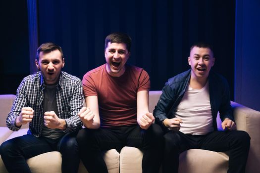 Male best friends spending time together. Three best friends watching sport competition on tv at home, enjoying good game. Joyful guys laughing.