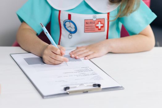 Young female medical working in medical center. Hands of beautiful little girl with notepad sitting at the wooden table and writing notes