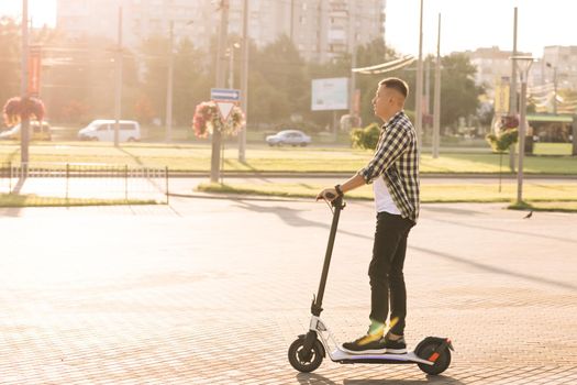 Young smart hipster man riding a fast modern electric scooter near huge contemporary construction in open landscape on country road. Eco transportation. Fast speed driving electric transport.
