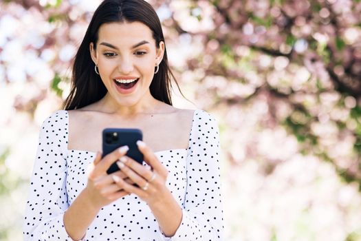 Closeup joyful girl reading good news on phone. Surprised lady celebrating victory on phone. Portrait of happy woman enjoy success on mobile phone.