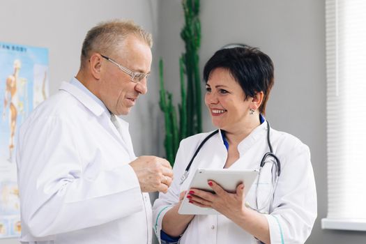 Medical team two old male and young female doctors wear white coats talk, use digital tablet. Two Hospital Partnership in medicine concept, healthcare tech. Close up view