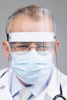 Doctor in Glasses is Wearing a Transparent Protective Face Shield, Mask and Overalls in a Hospital Room. Covid-19 Pandemic Concept About Slow Spread of Infectious Virus