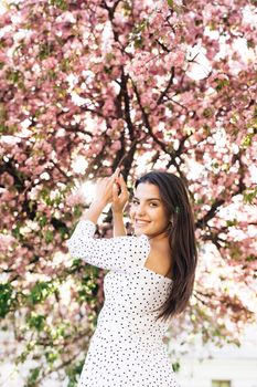 Gorgeous young woman with beautiful brown eyes and long hair, with a bright pink lipstick. Attractive young lady is walking down the city street park, turns to camera and gives a lovely playful smile.