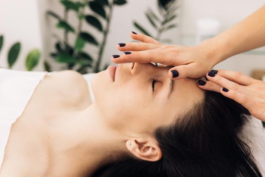 Woman lying on spa bed get facial massage treatment with aroma essential oil skincare from massage therapist at beauty salon. Wellness body massage and face spa concept