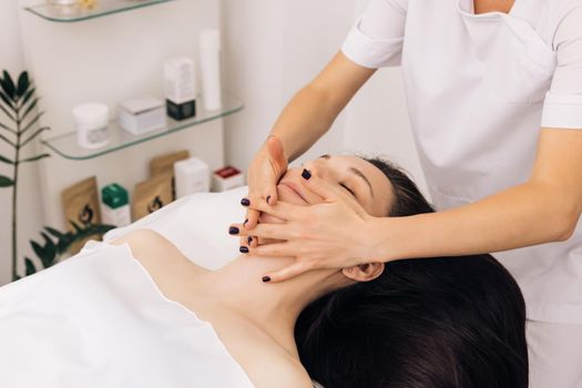 Face Massage in beauty spa salon. Caucasian woman receiving a facial massage at an aesthetic salon. Spa facial Massage. Body care, skin care, wellness, wellbeing, beauty treatment concept.