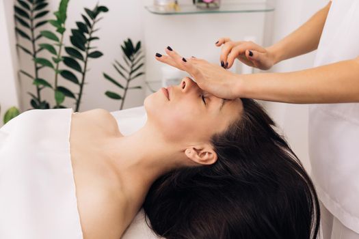 Close up of young girl receiving a facial massage and spa treatment for perfect skin in a luxury wellness center. Caucasian woman lying on spa bed get facial massage from massage therapist at clinic.