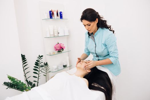 Young woman having massage by a female masseur in blue medical pijama at modern health center. Wellness health concept. Woman relaxing during massage lying on massage table.