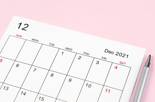 Close up December 2021 calendar sheet with pen on pink background.