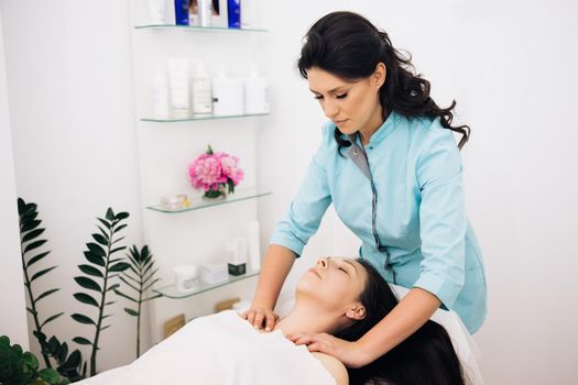 Woman relaxing during massage lying on massage table. Young woman having massage by a female masseur in blue medical pijama at modern health center. Wellness health concept.