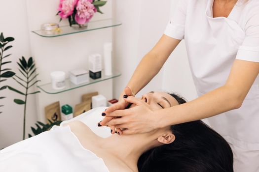 Wellness, stress relief and rejuvenation concept. Relaxed woman lying on spa bed for facial and head massage spa treatment by massage therapist in a luxury spa resort.