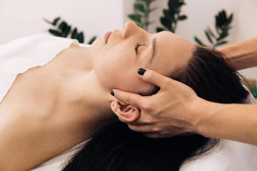 Beautician doctor is applying facial cleansing foam on woman's face massaging skin in cosmetology clinic. Cosmetologist making skin care procedure in beauty salon, portrait of girl closeup.