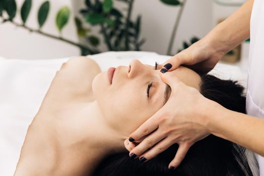 Caucasian woman lying on spa bed get facial massage treatment with aroma essential oil skincare from massage therapist at beauty salon. Wellness body massage and face spa concept