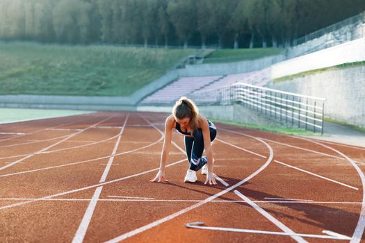 Female athlete training at running track in the morning light. Young woman runner preparing for blasting off in mist on sports track of stadium. Athlete ready to start. Sportswoman. Cardio exercises.