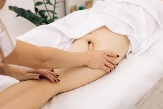 Professional is massaging and touching skin of female client, using traditional techniques. Specialist works with body of patient. Masseur is doing massage of back of woman lying in beauty salon.