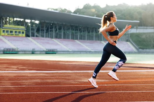 Female sprinter race on outdoor track arena. Female marathon runner on professional sports arena. Fitness woman racing at stadium. Motivated girl winning speed contest.