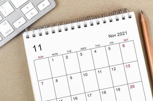November 2021 desk calendar with pencil on wooden background.