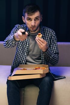 Man eating Italian food. Relaxation cinema channels resting. Young hipster man eating pizza, watching favorite film on tv while relaxing at sofa in the living room.