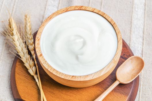 Greek yogurt in a wooden bowl and dry barley on tablecloth.