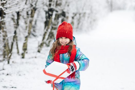 Little girl with christmas box gift in winter outdoors on Xmas eve. Happy Little caucasian girl smile and holding gift box in Christmas day. Child holding gift box and surprise face.