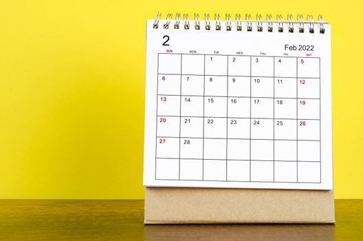 February 2022 desk calendar with yellow background on the wooden table.