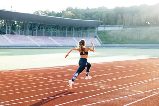 Caucasian woman running in sportswear doing cardio workout on sports track of stadium. Adult female athlete jogging, training before marathon competition. Health. Sportswoman