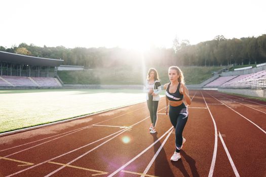 Female runner with personal trainer preparing for blasting off in mist on sports track of stadium, training before competition. Caucasian Athlete ready to start. Sportswoman. Cardio exercises.