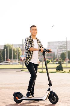 Stylysh man on vehicle outdoors. Male in city in sunlight on sunset. Eco-friendly modern urban transport. Portrait shot of caucasian hipster man leaning on electric scooter and looking at camera.