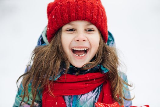 Close up of the happy cute girl looking at the camera and smiling the background of a snowy forest. Positive child. Portrait shot. Outside. The dead of winter, cold weather, frost, snow.