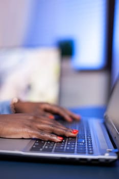 Close up of african worker hands typing on laptop computer keyboard in home office. Employee using modern technology network wireless doing overtime.