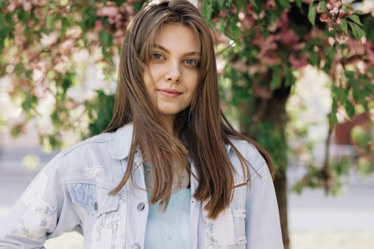 Portrait of young mixed race beauty american woman with long hair style standing on street near sakura trees, looking friendly at camera. Human face, ideal natural make up skin concept