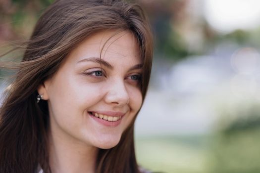 Close up portrait Smiling attractive young adult woman model, happy beautiful 20s brunette lady pretty face dental smile posing stand alone at park on a background of sakura trees.