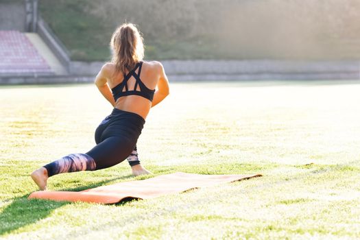 Young caucasian fit sport woman stretching her body warm up before workout outdoor. The girl in sportswear exercises outside in the morning sun for health and wellbeing.