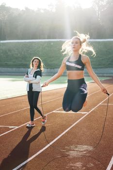 Athletic woman with personal instructor skipping rope as part of her fitness workout. Sporty female with a good figure jumps rope on sports track of stadium. Exercising strength cardio and power.