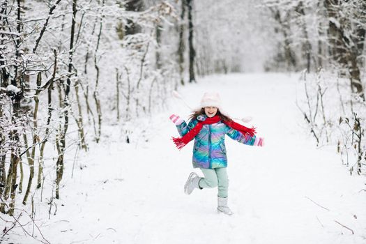 Funny laughing child girl running in a beautiful snowy park. Happy girl playing on a winter walk in nature. Expressing positivity, true brightful emotions, smiling.